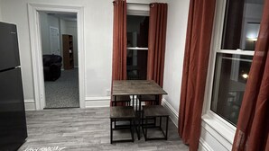 A compact kitchen with a dining table, a refrigerator, and a window with curtains.