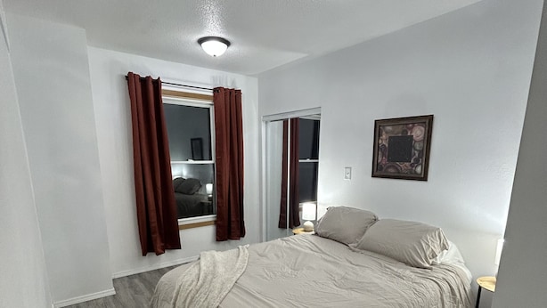 A bedroom with a bed, a window with curtains, a bedside table, and a wall-mounted picture.