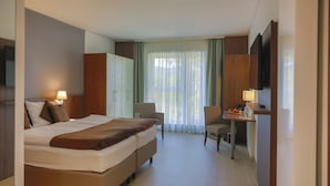 A hotel room with a large bed, a desk, a chair, and a wardrobe. - Sporthotel Treff Punkt (Wiesbaden)