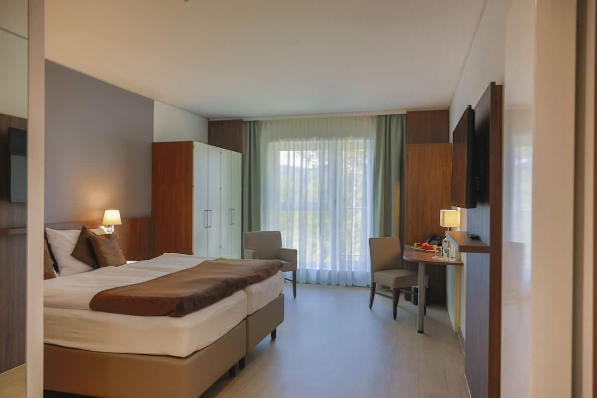A hotel room with a large bed, a desk, a chair, and a wardrobe.