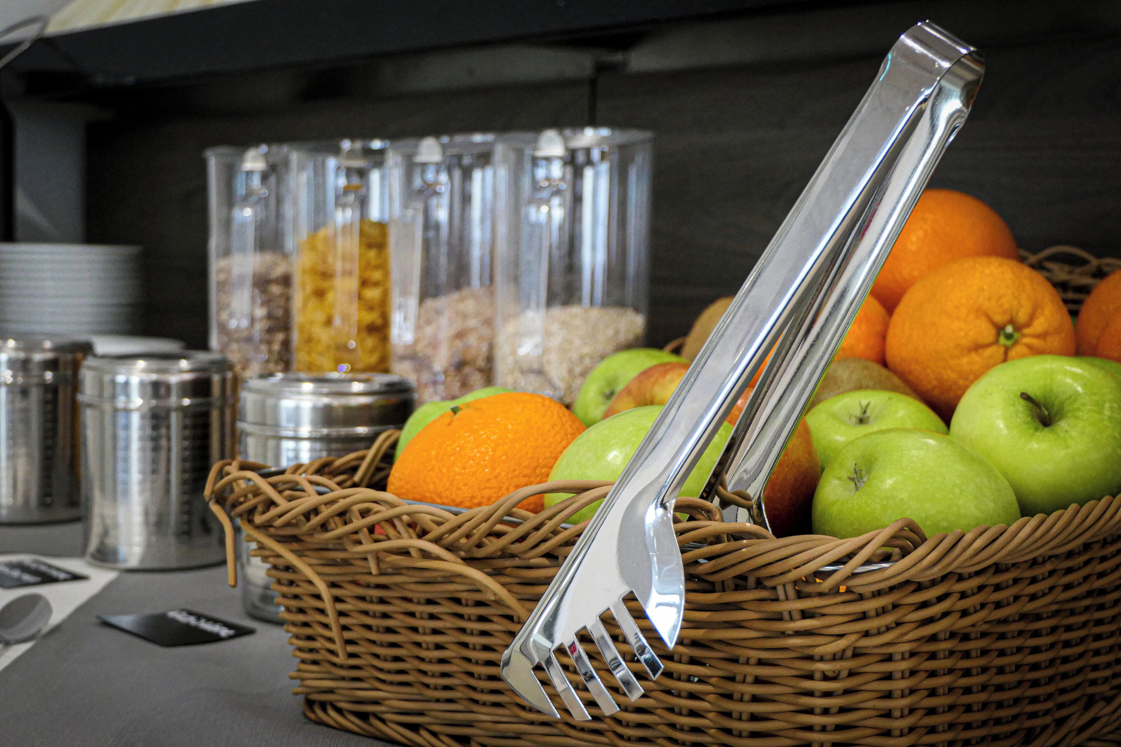 A wicker basket filled with fruits and a metal fork and knife.
