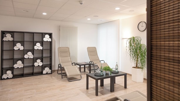 A modern waiting area with a sofa, two recliners, a coffee table, a bookshelf, and a potted plant. - Sporthotel Treff Punkt (Wiesbaden)