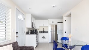 A modern kitchen with white cabinets, stainless steel appliances, and a glass dining table with blue chairs.