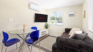 A modern living room with a glass dining table, blue chairs, a dark brown sofa, and a mounted TV displaying 'NETFLIX'.