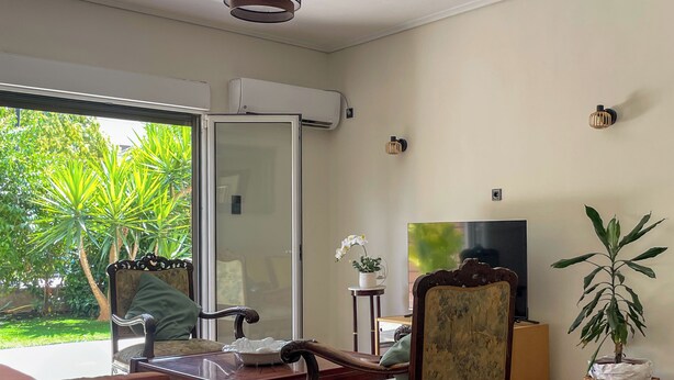 Un soggiorno con una porta vetrata che si apre su un giardino, un tavolino in legno, una poltrona, un televisore e una pianta in vaso.
