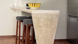 Una cucina con un piano di lavoro bianco, una ciotola di banane e due sgabelli di legno.