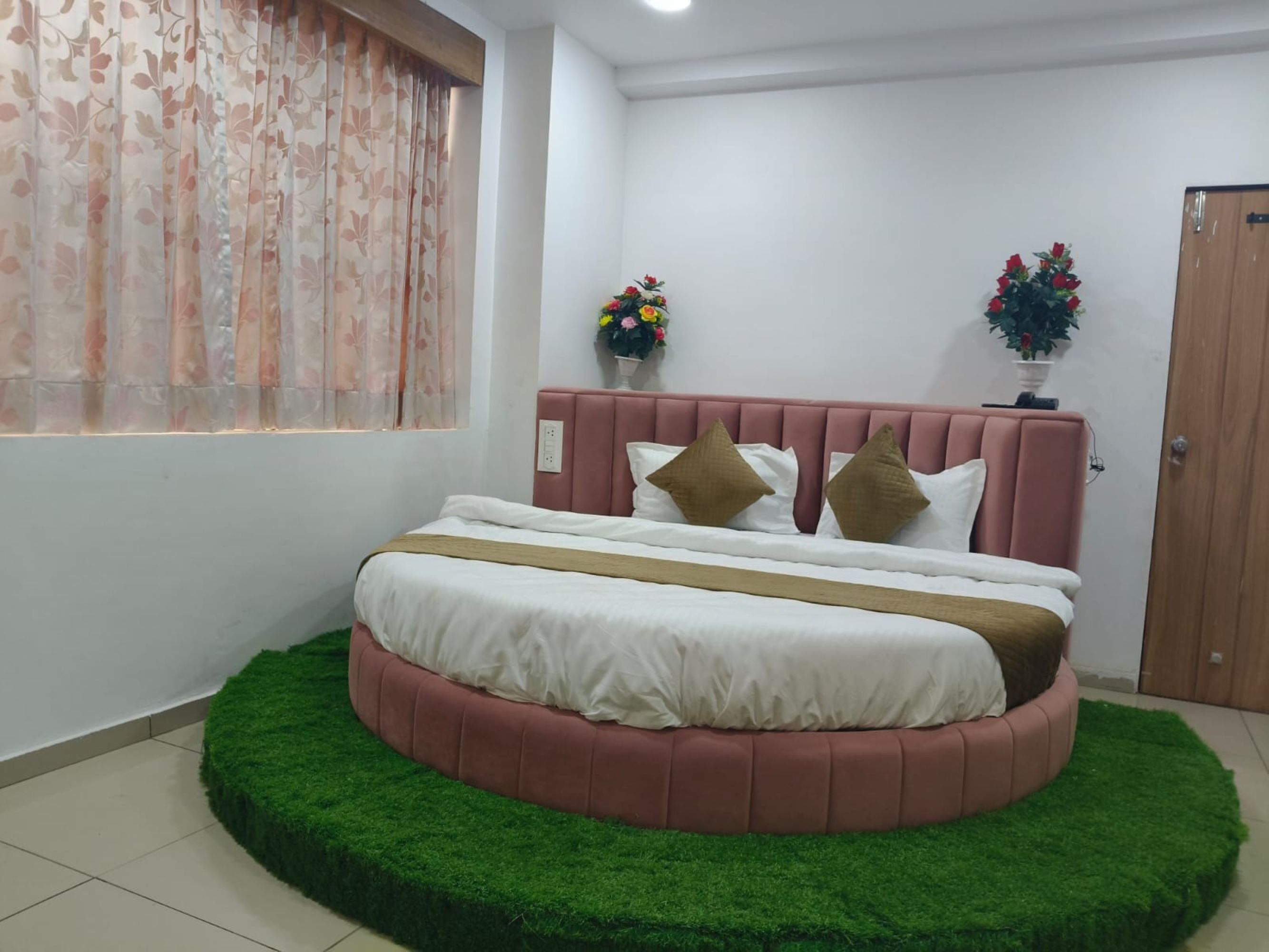 A bedroom with a circular bed, a pink headboard, and a green rug.