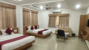 A hotel room with two beds, a desk, a chair, an air conditioning unit, and a ceiling fan.