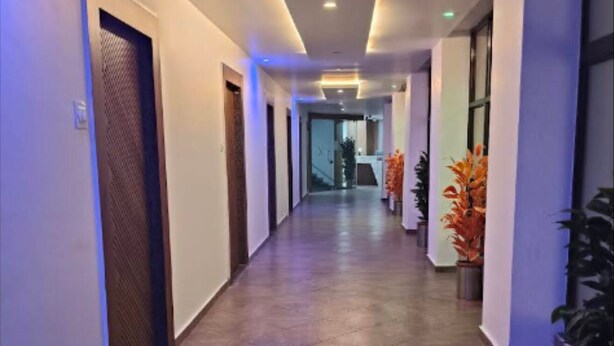 A long, narrow hallway with tiled flooring, doors on both sides, and potted plants along the right wall.