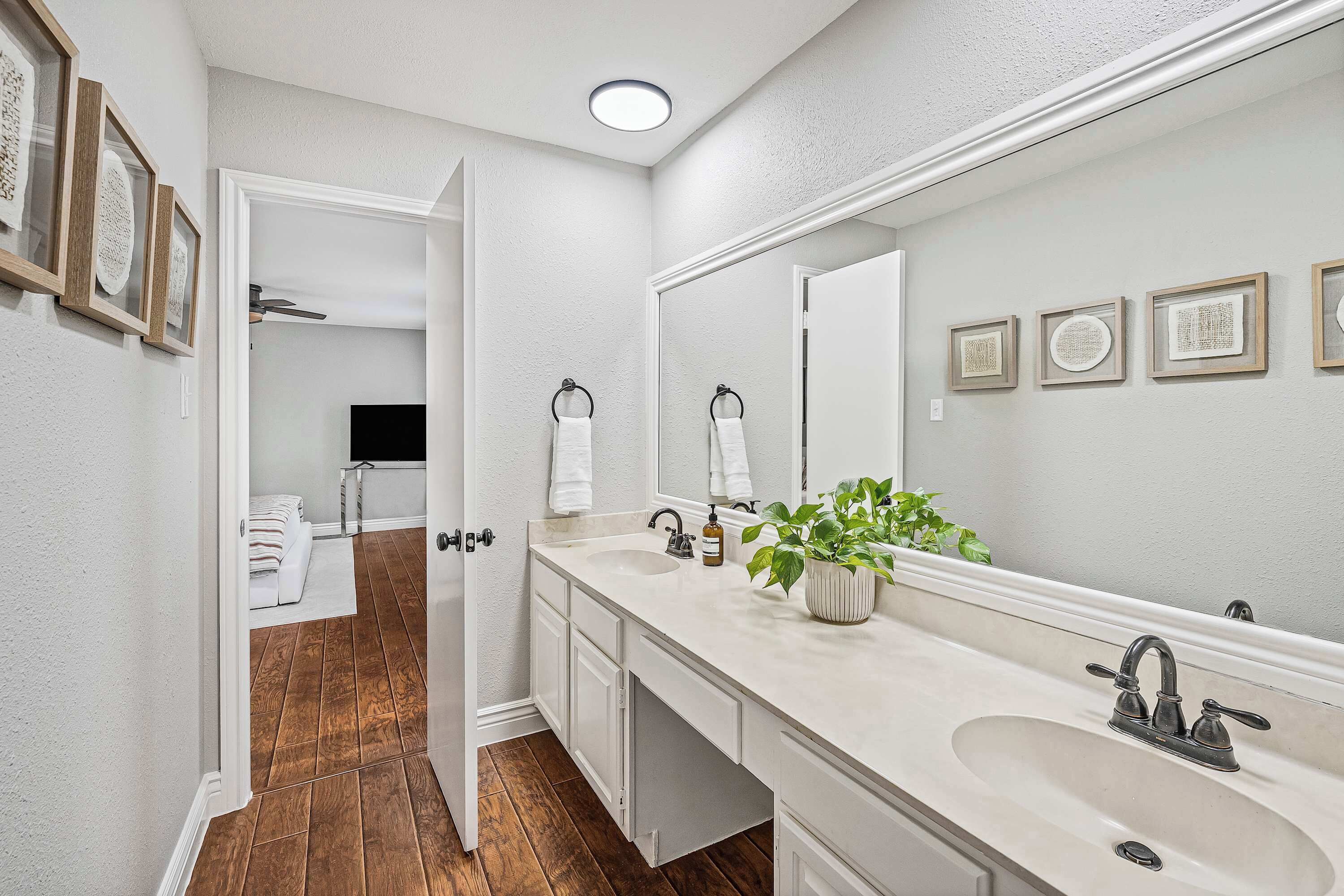 A bathroom with a white vanity, a large mirror, and framed artwork on the wall.