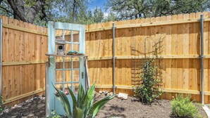 Une cour arrière clôturée, avec une clôture en bois, une mangeoire à oiseaux et quelques plantes.