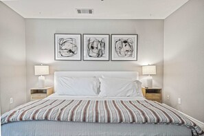 Une chambre à coucher avec un lit, deux tables de chevet et trois tableaux abstraits accrochés au mur.