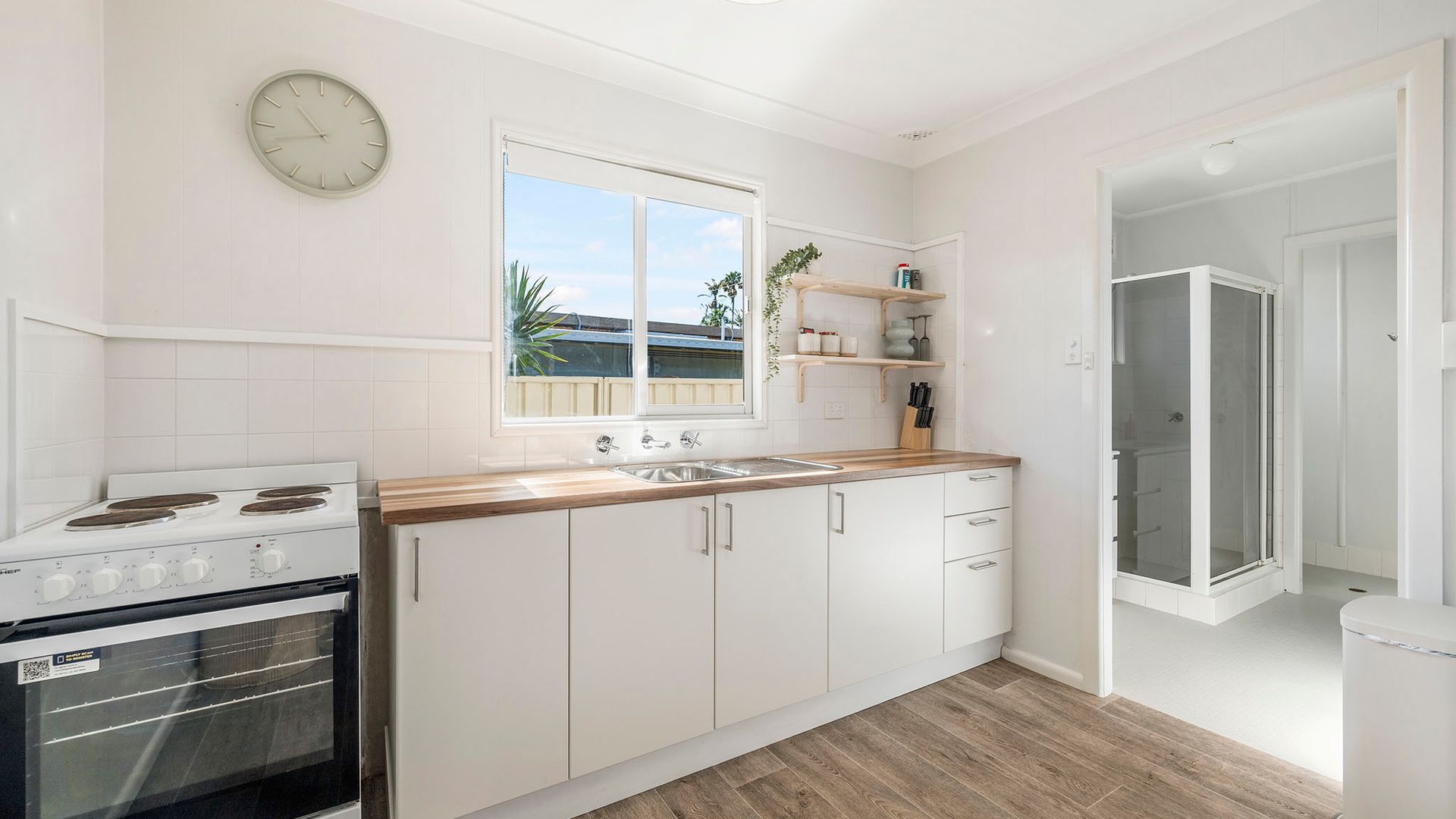 A modern kitchen with white cabinetry, a wooden countertop, a built-in oven, and a window with a view of the outside.