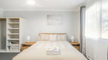 Un dormitorio con cama, mesitas de noche, un armario y una ventana con cortinas.