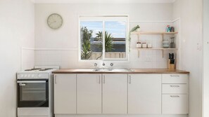 Una cocina con armarios blancos, estufa, lavaplatos y ventana con vistas al exterior.