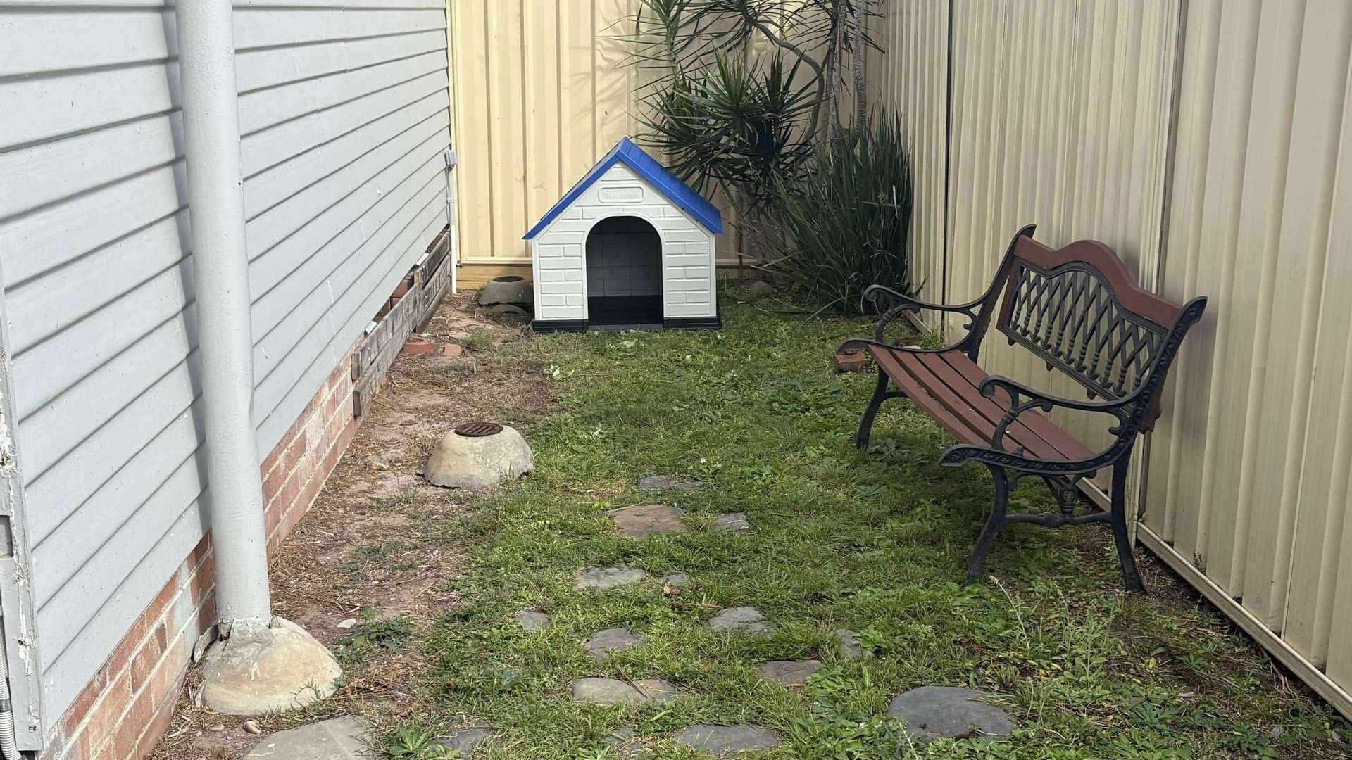 A small outdoor area with a doghouse, a bench, and a paved path.