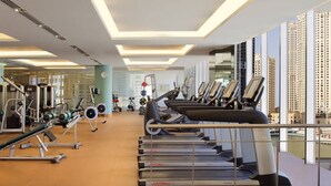 Une salle de sport moderne équipée de tapis de course, d’appareils de musculation et dotée d’une grande fenêtre offrant une vue sur la ville.