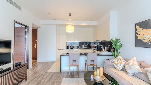 Una sala de estar moderna con un sofá, una mesa de centro y un televisor. Se ve una cocina al fondo, junto con una zona de comedor.