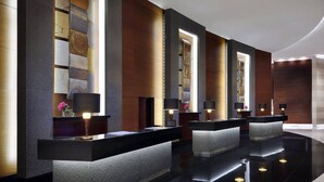 Un área de recepción moderna con un mostrador negro, un espejo grande y una pared con paneles de madera y una lámpara.