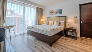 Una habitación de hotel moderna con una cama grande, lámparas de noche, un escritorio y vistas de la ciudad a través de amplias ventanas.