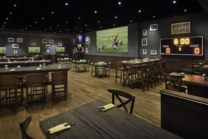 A sports bar with multiple seating areas, a large screen displaying a football game, and a digital scoreboard. - Exclusive Dubai Marina Life - Sun Sand Dining (Dubai)