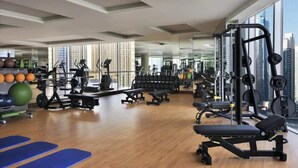 Une salle de sport équipée de matériel d’exercice, de miroirs et de grandes fenêtres donnant sur un panorama urbain.