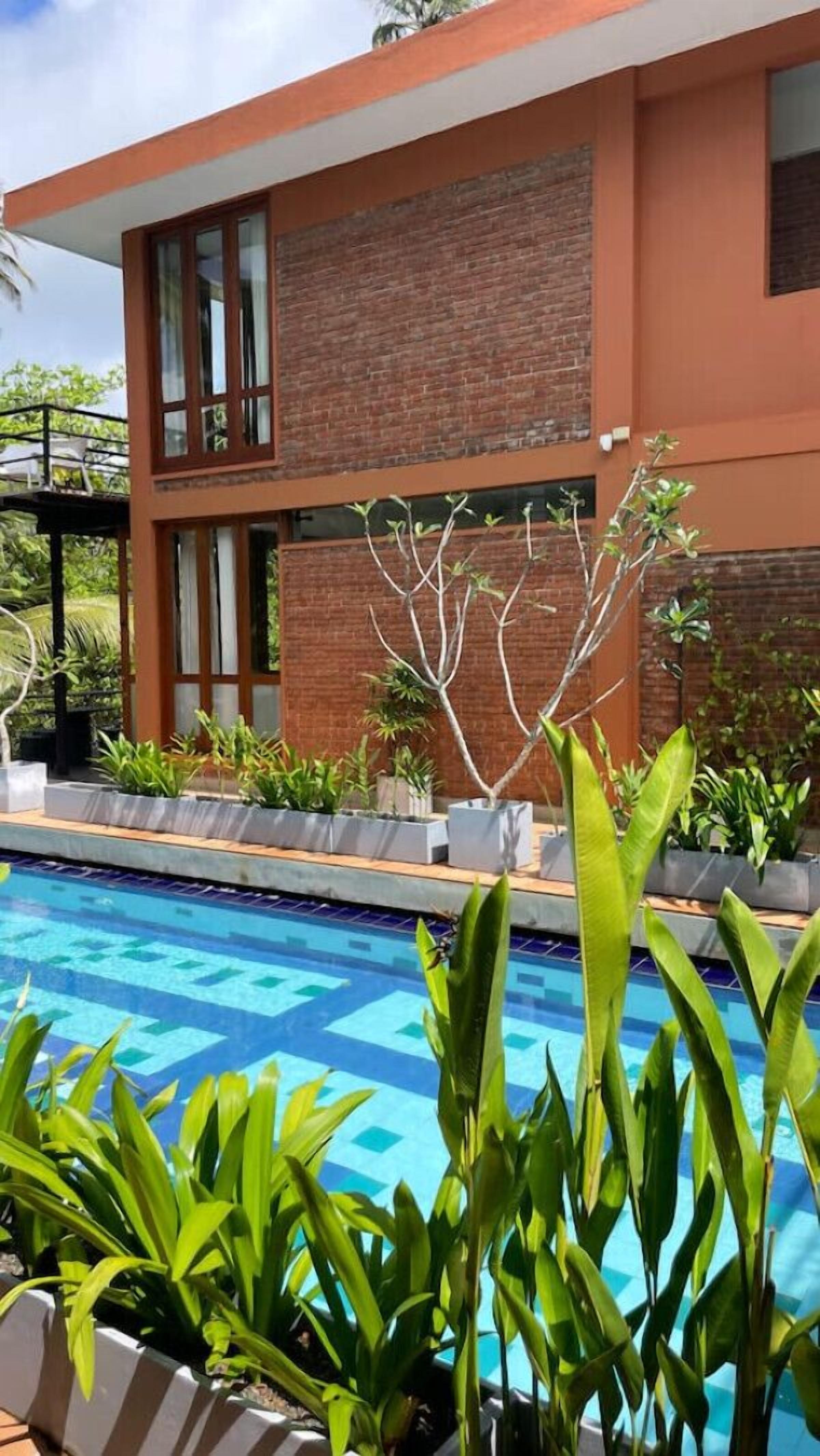 A modern two-story building with a brick facade and large windows. In front of the building is a swimming pool with a blue tiled pattern.
