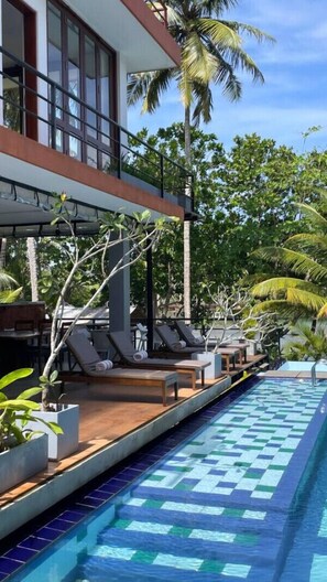 Un área junto a la piscina con sillones de descanso y una piscina con azulejos azules.
