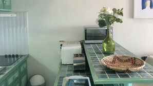 A kitchen with a green countertop, a toaster, a microwave, a trash bin, and a vase with flowers. - Charming Apartment in Creole Village of Trois-Ilets (Les Trois-Îlets)