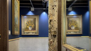 An art gallery with framed paintings on the walls, a textured stone column, and a wooden door.