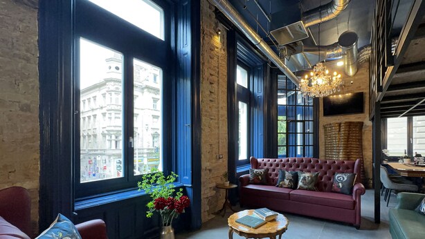 A spacious living area with a red sofa, a small wooden coffee table, and a large window offering a view of a building.