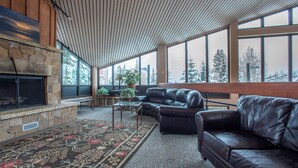 A spacious living room with a stone fireplace, leather sofas, and large windows offering a view of snow-covered trees. - Beautiful Ski-in/Ski out Center Village studio, sleeps 4 (Copper Mountain)