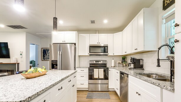 A modern kitchen with white cabinets, granite countertops, stainless steel appliances, and a large island with a bowl of fruit. - 5 Mi to Dtwn Atlanta: Family Home w/ Fenced Yard (Atlanta)