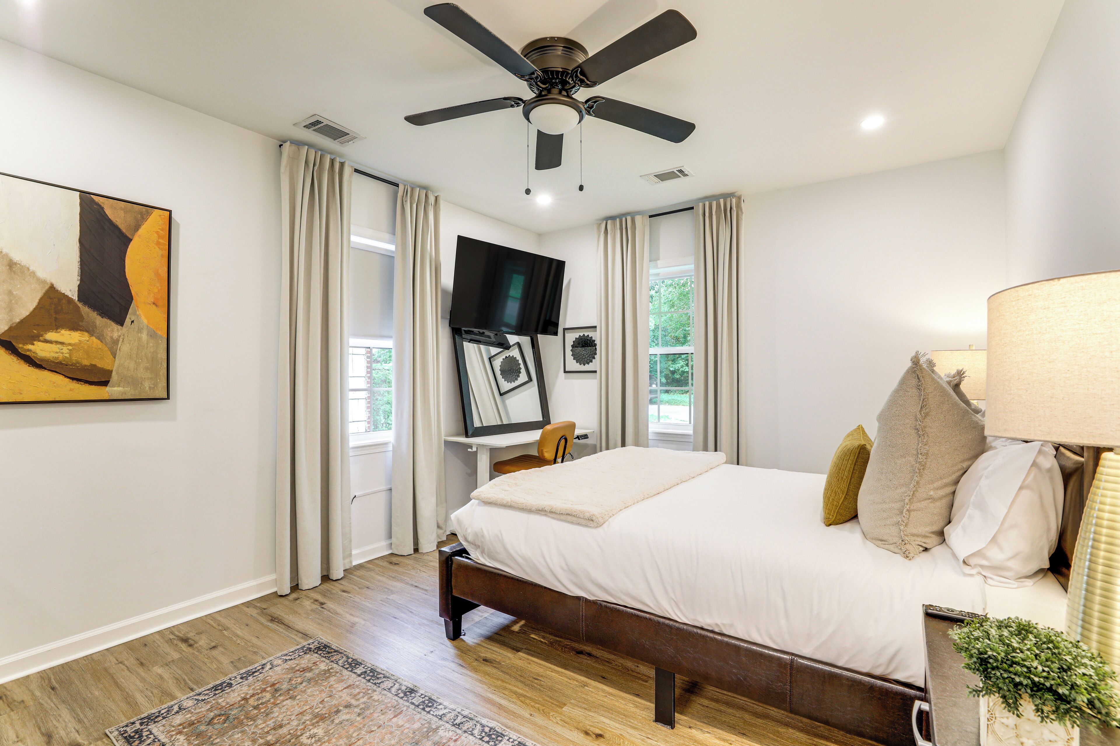 A bedroom with a bed, a ceiling fan, a TV, and a window with curtains.