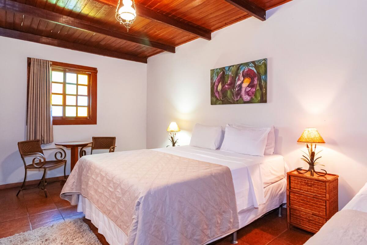 A bedroom with a bed, two bedside tables with lamps, a chair, a small table, and a window with curtains.