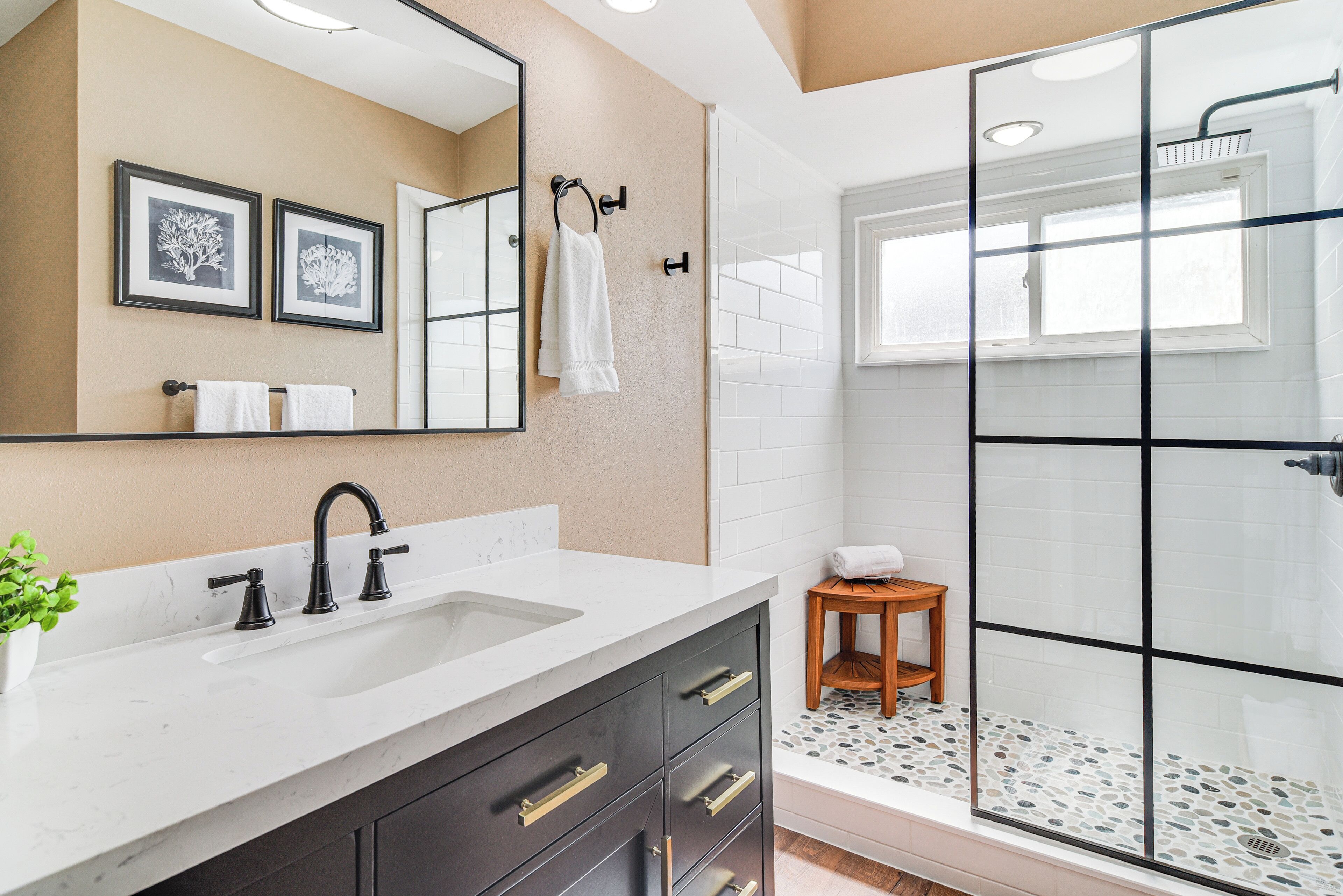 Un baño moderno con un espejo grande, un lavamanos blanco, armarios oscuros y una zona de ducha con mampara de cristal.