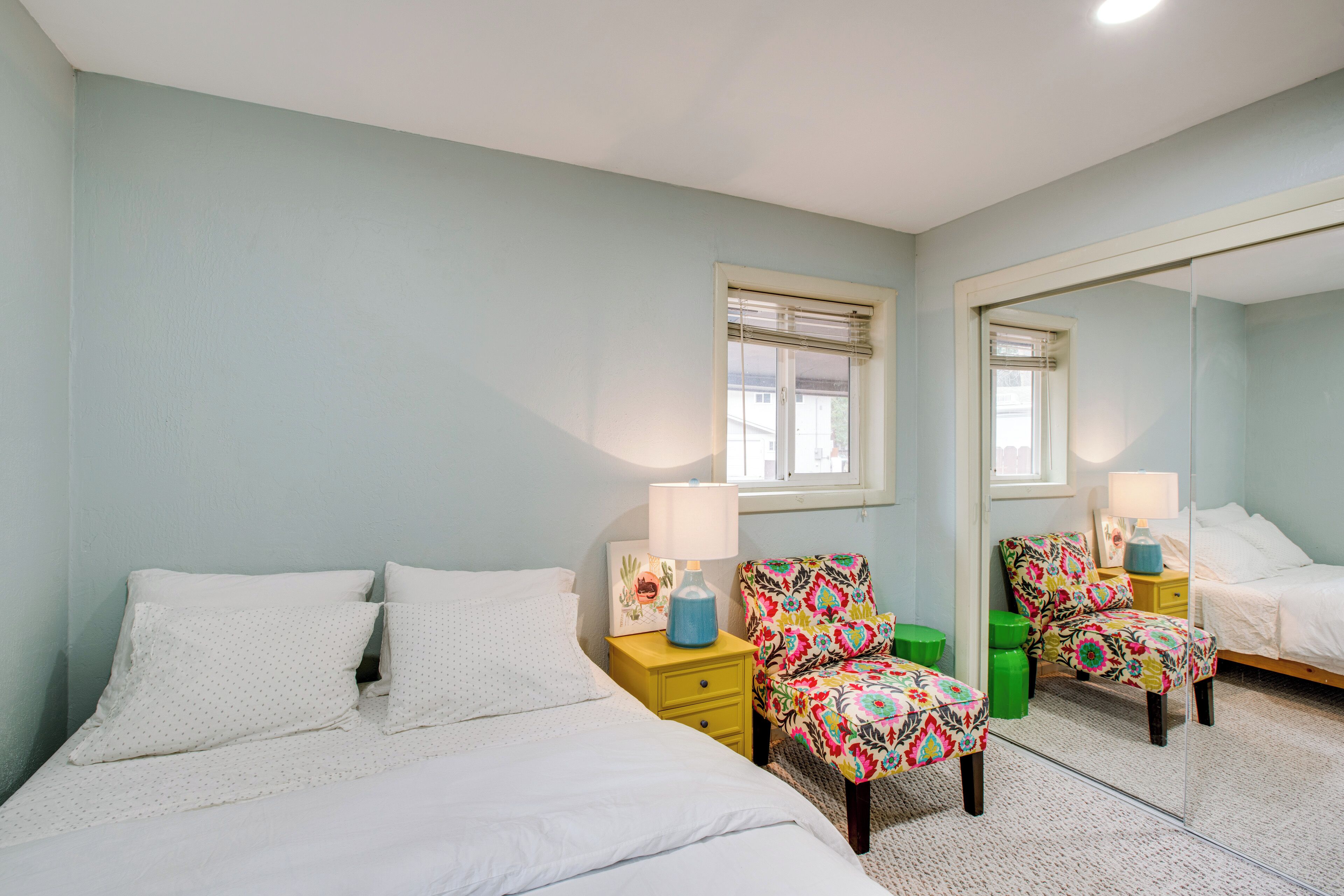 A bedroom with a bed, two nightstands, a mirror, and a window with blinds.