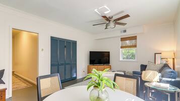 A modern living room with a dining table, chairs, a sofa, a TV, and a ceiling fan.