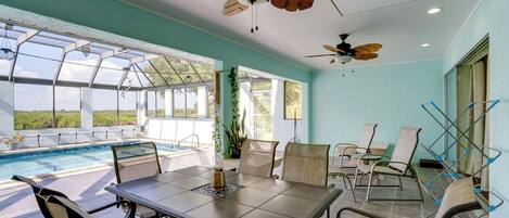 A sunlit room with a pool, a table with chairs, and ceiling fans.