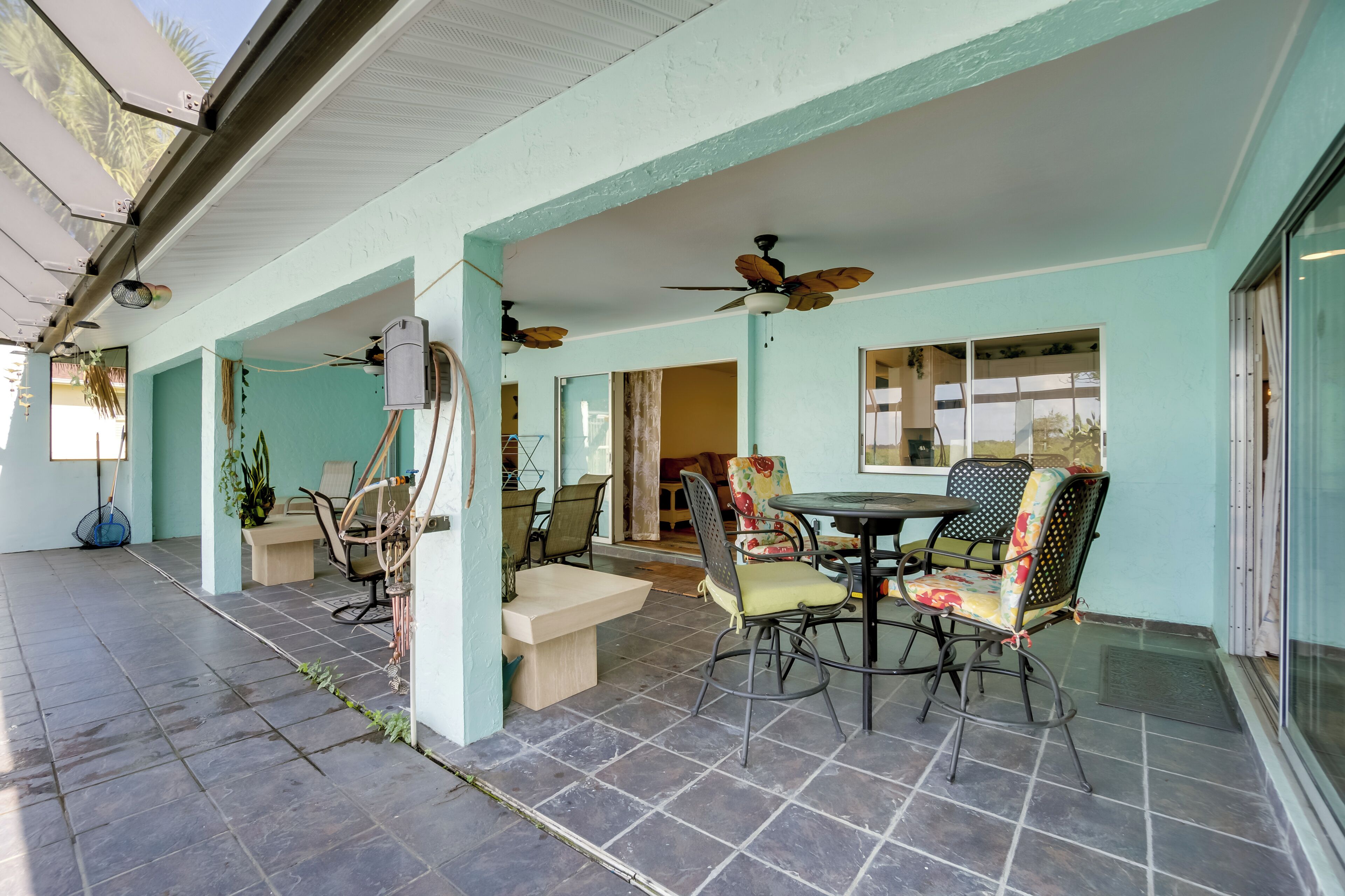 A covered patio area with tiled flooring, ceiling fans, and outdoor seating with chairs and a table.