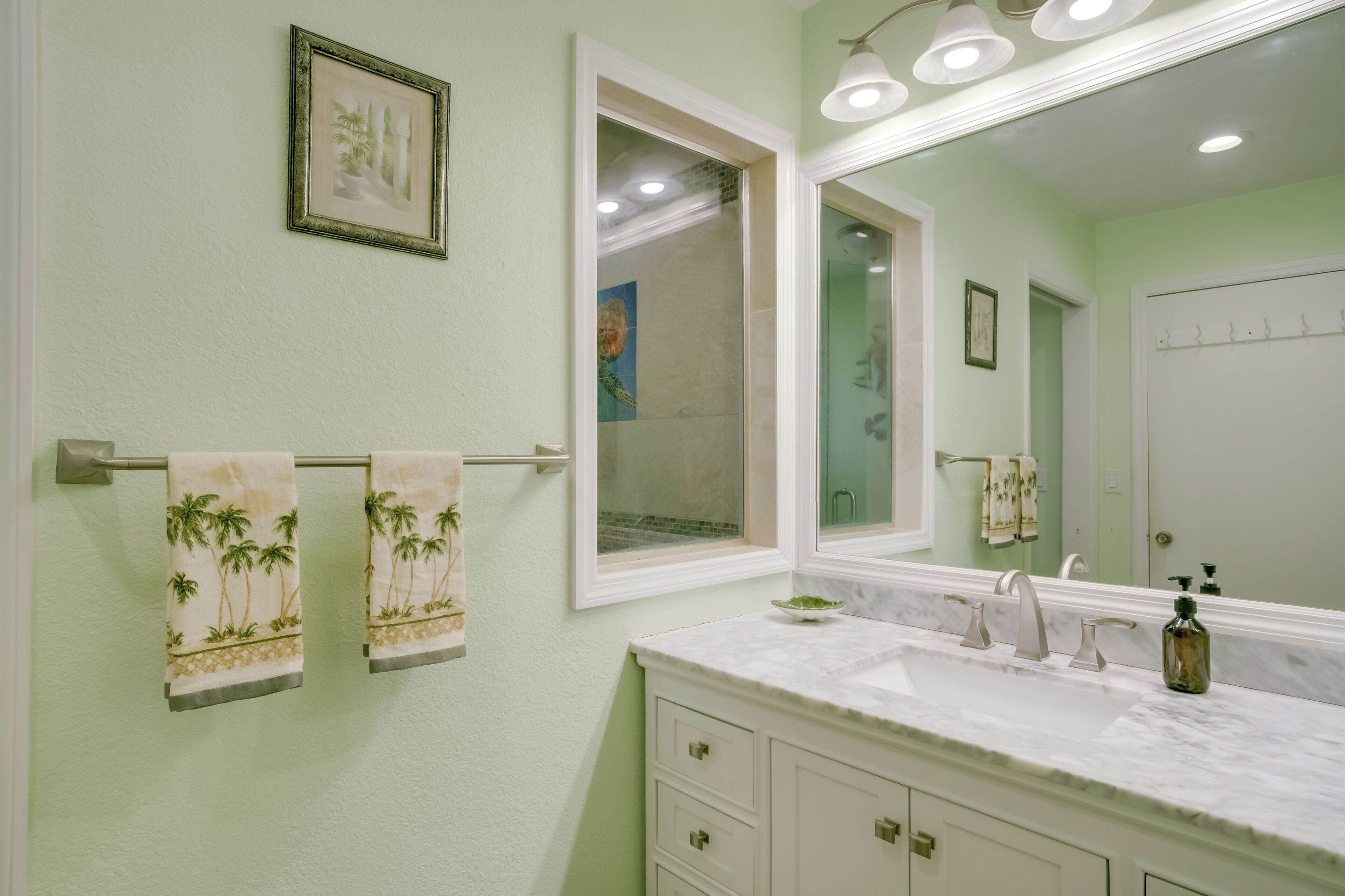 A bathroom with a white vanity, a large mirror, and two towels with palm tree designs.