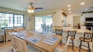 A spacious kitchen with a large island, wooden dining table with blue placemats, and a ceiling fan. - Heated Pool + Lanai: Peaceful Punta Gorda Stay (Punta Gorda)