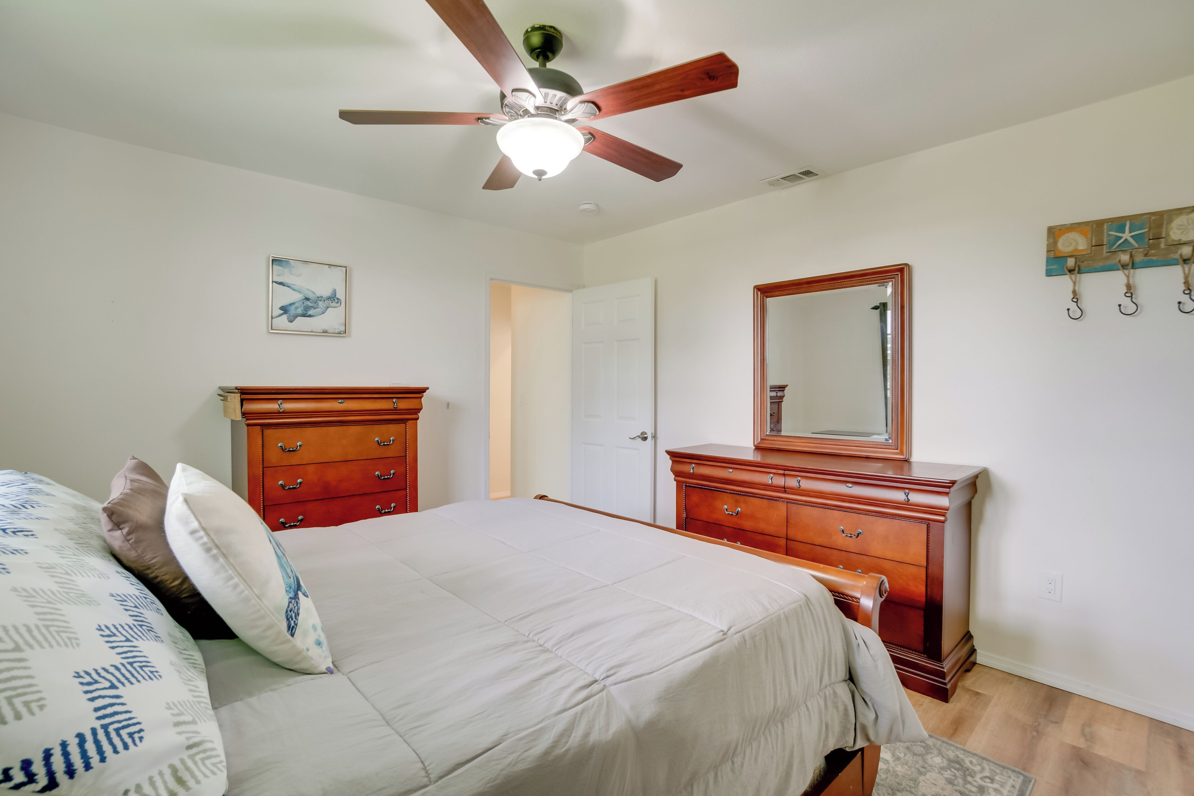 A bedroom with a bed, wooden dresser, and a ceiling fan.