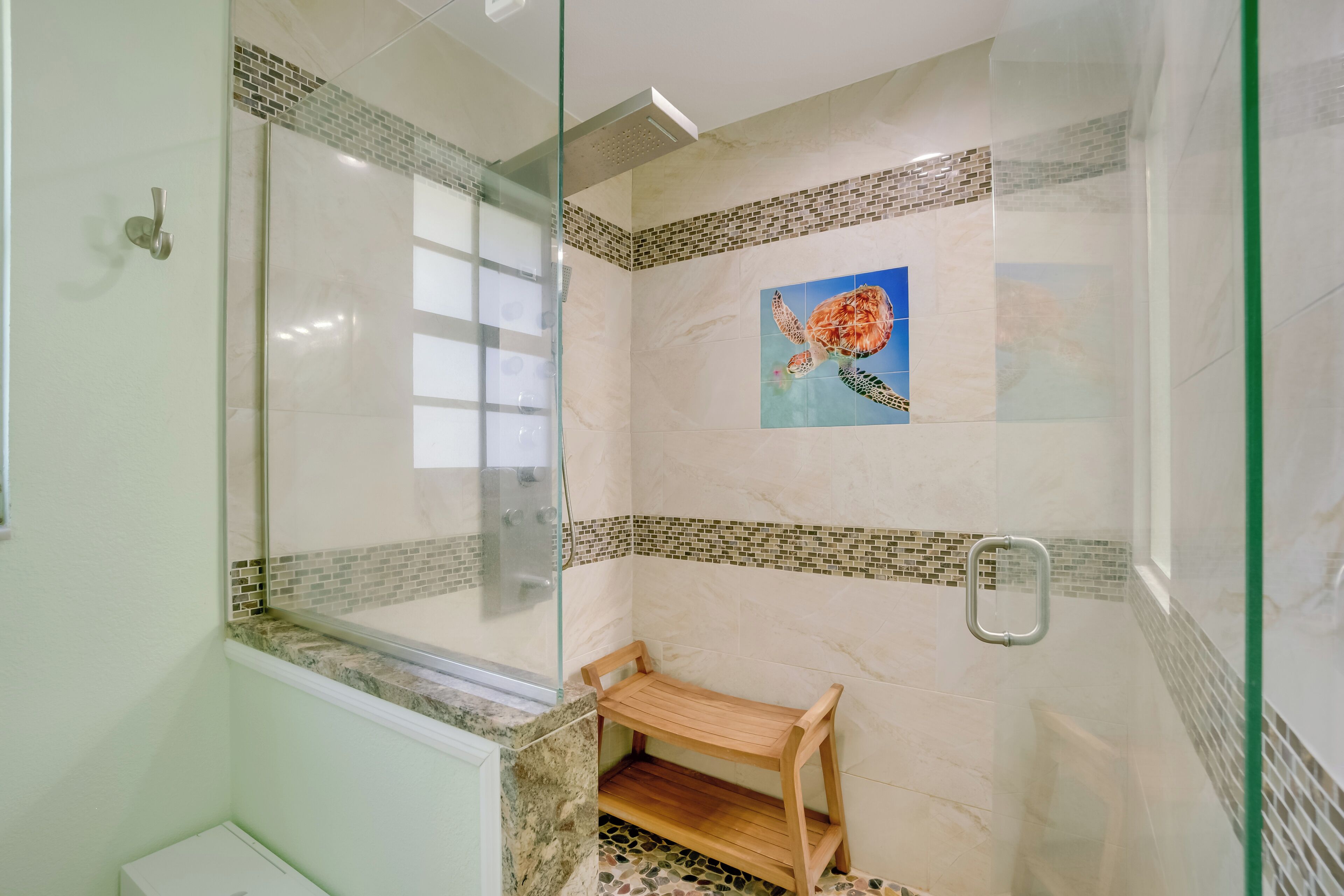 A shower area with a glass door, a wooden bench, and a mosaic tile design on the walls.
