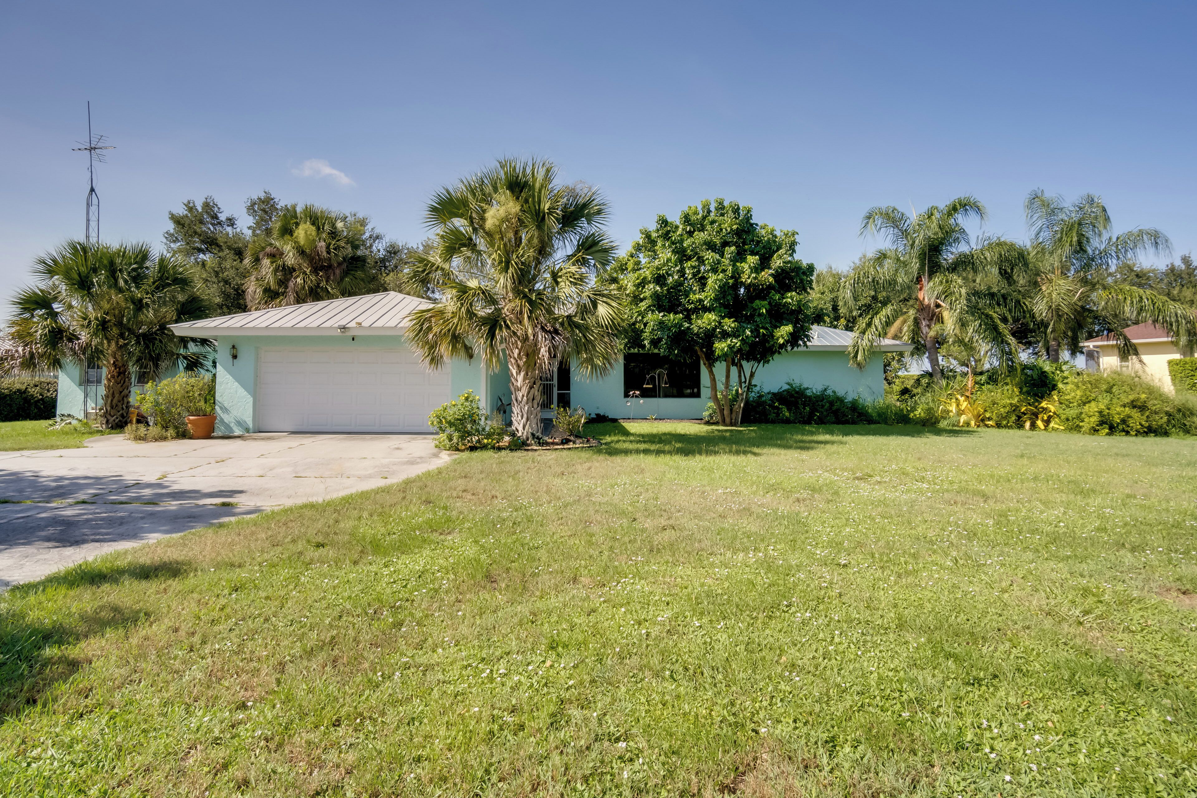 A single-story house with a garage, surrounded by a well-maintained lawn and palm trees.