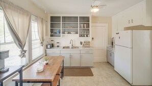 Une cuisine de taille réduite avec des meubles blancs, une table en bois, un évier et un réfrigérateur.