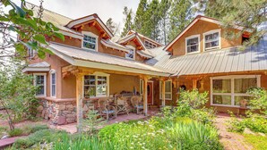 A two-story house with a stone foundation, a covered patio with outdoor furniture, and a garden with various plants and flowers. - Steps From Natl Forest: Creekside Home in Durango (Durango)