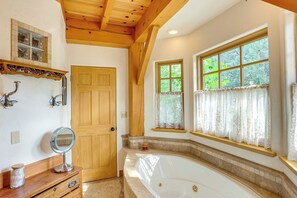 Un bagno con una porta in legno, un mobile toilette con uno specchio, una vasca da bagno e finestre con tende in pizzo.