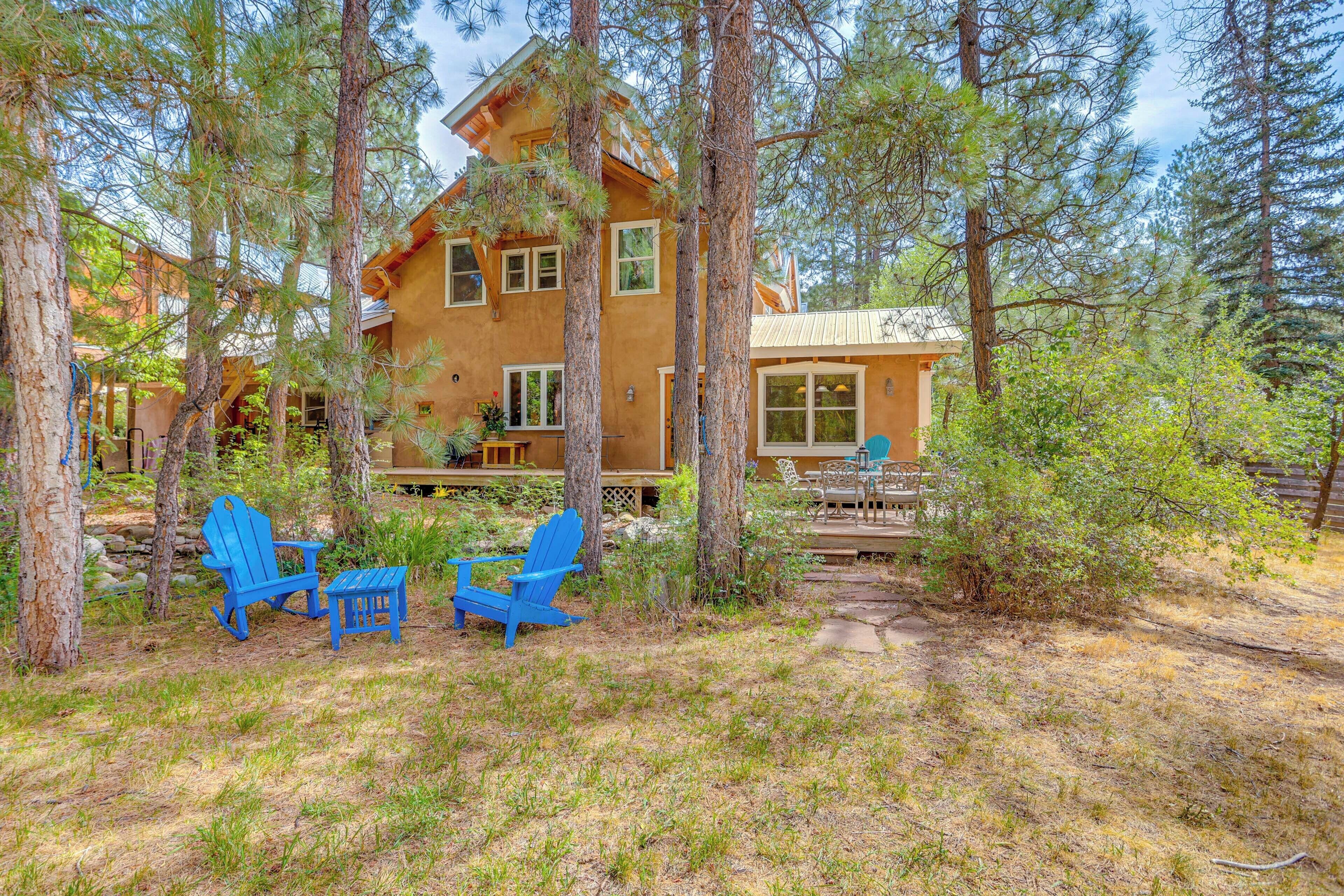 A rustic cabin with a deck, surrounded by tall pine trees.