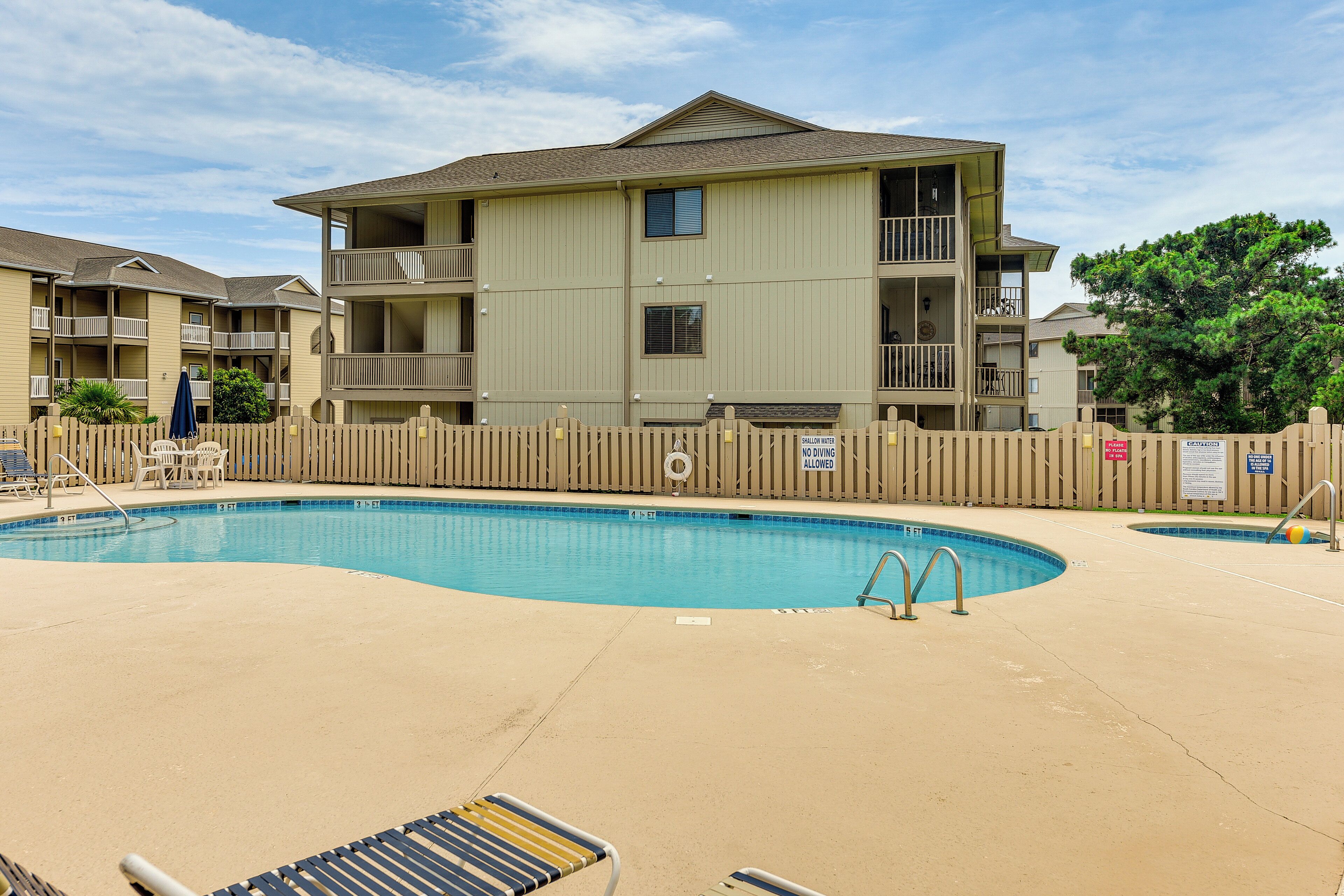 A swimming pool with lounge chairs and a wooden fence.